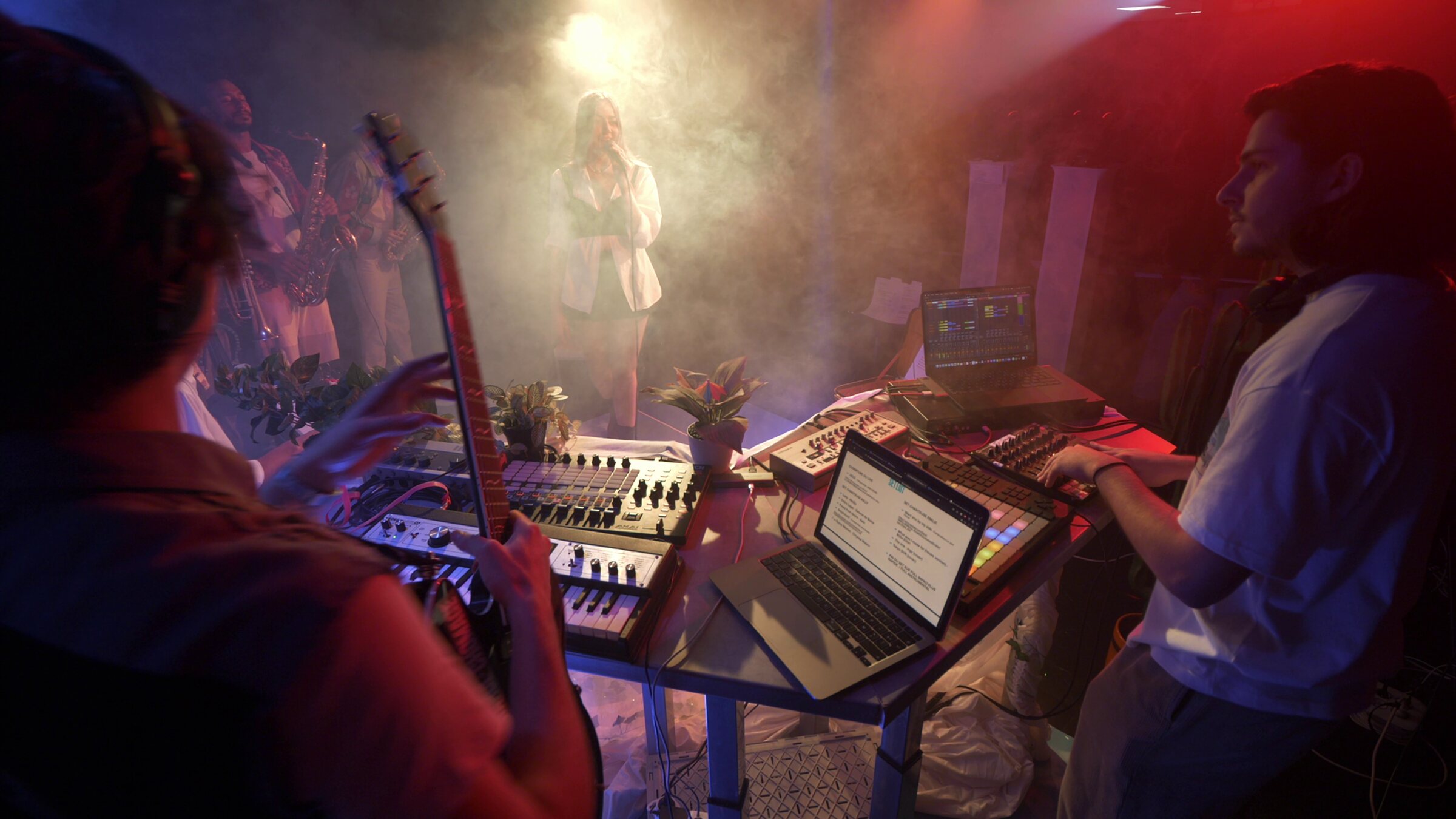 Session live filmée sous les projecteurs, chanteuse au micro et musiciens autour de la régie